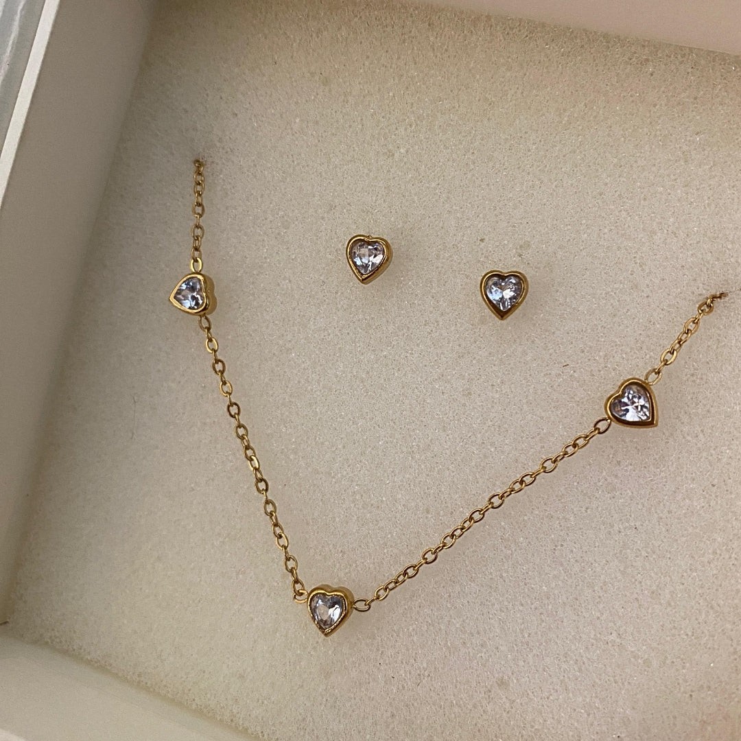 Close-up of heart-shaped clear stones in gold-tone settings on a necklace and matching studs