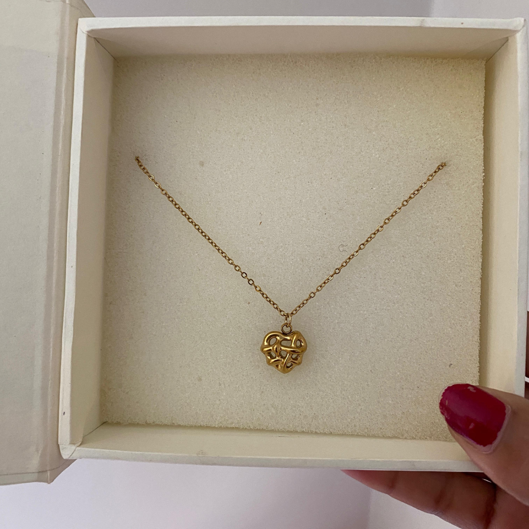  Close-up of a sculpted open-work gold-tone heart pendant on a stainless steel chain
