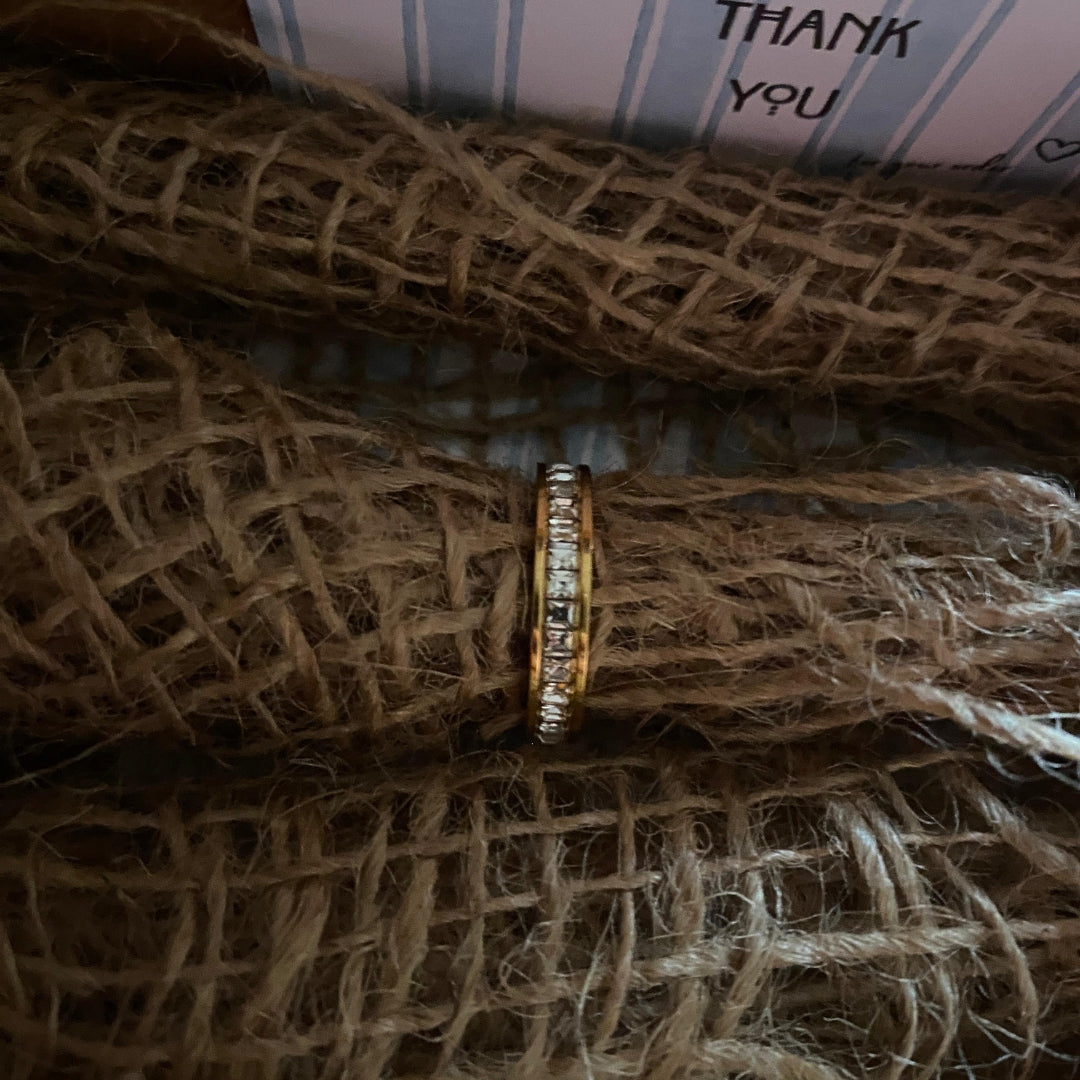  Close-up of square-cut clear stones in a single row on a gold-tone stainless steel band ring