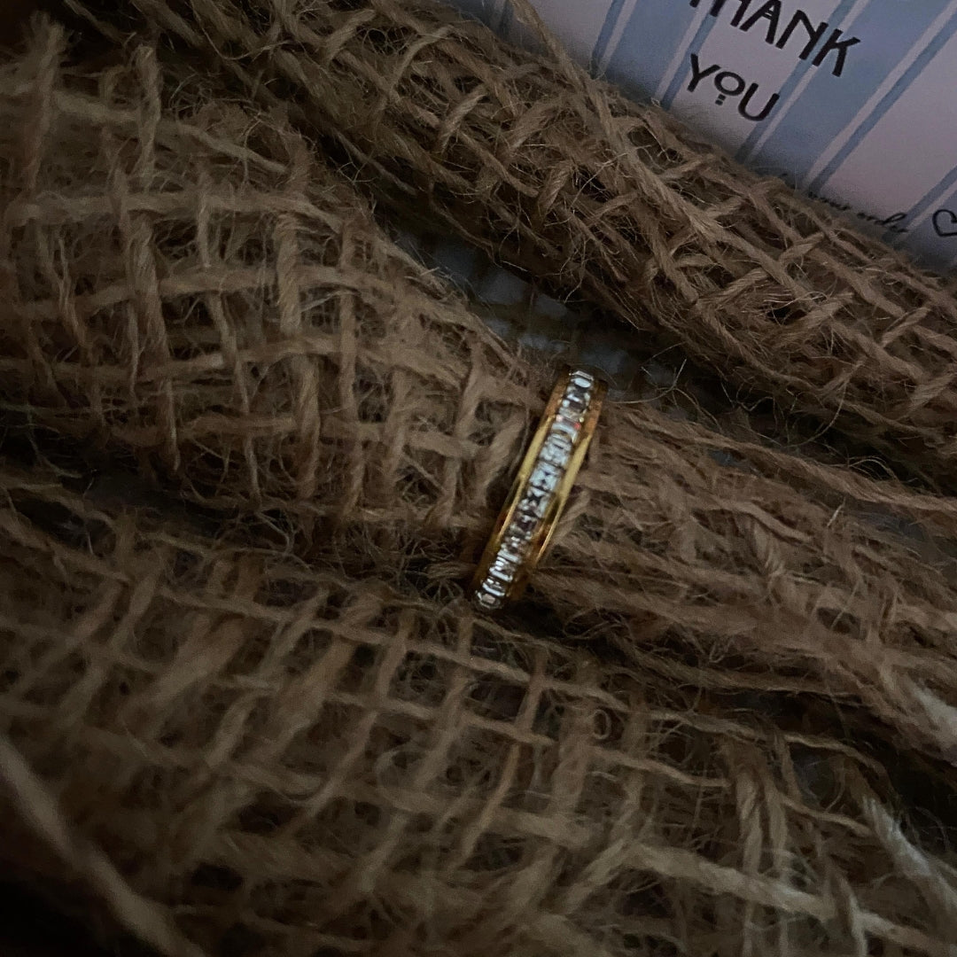 Angled view of a slim gold-tone stainless steel band ring lined with clear stones
